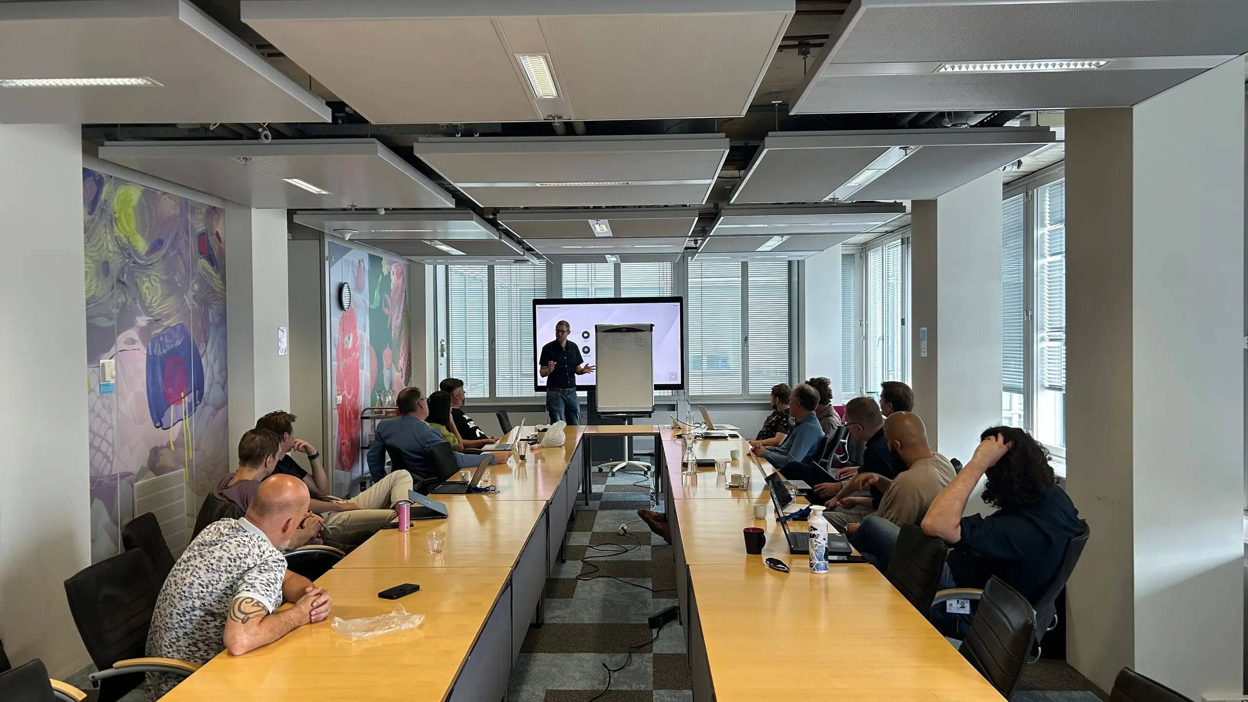 A DAWO working session: someone presenting beside a screen and a flip chart, with fourteen participants seated at tables around them.